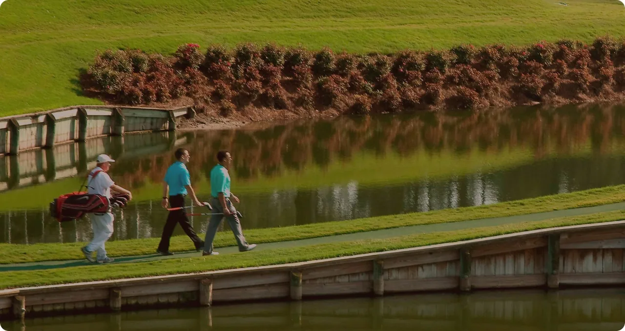 Golfers walking beside a Sawgrass course water feature.